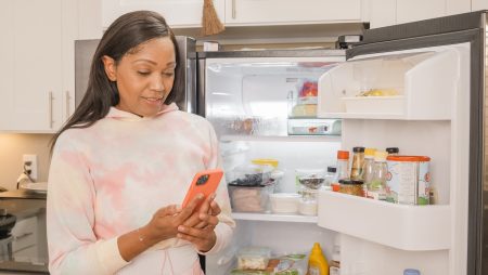 woman looking at phone near open fridge, frugal mum, recipe, leftovers ideas, budget food shop tips