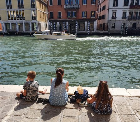 venice, photo of frugal mum and children enjoying picnic by the water, travelling on a budget tips, italy